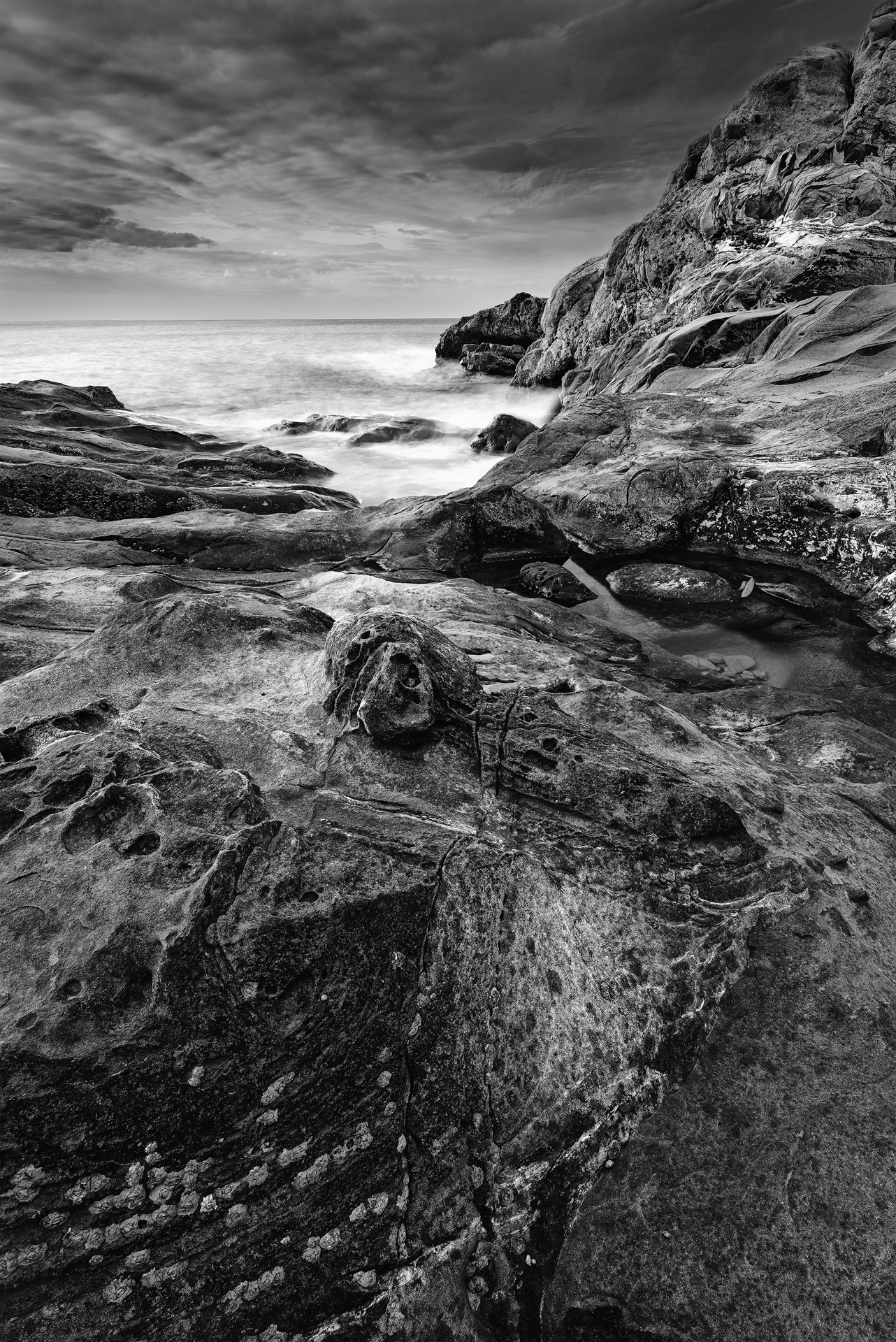Scogliera dalle forme scolpite dal tempo, con il mare in lontananza. Lunga esposizione che ammorbidisce le onde e valorizza i contrasti della roccia.