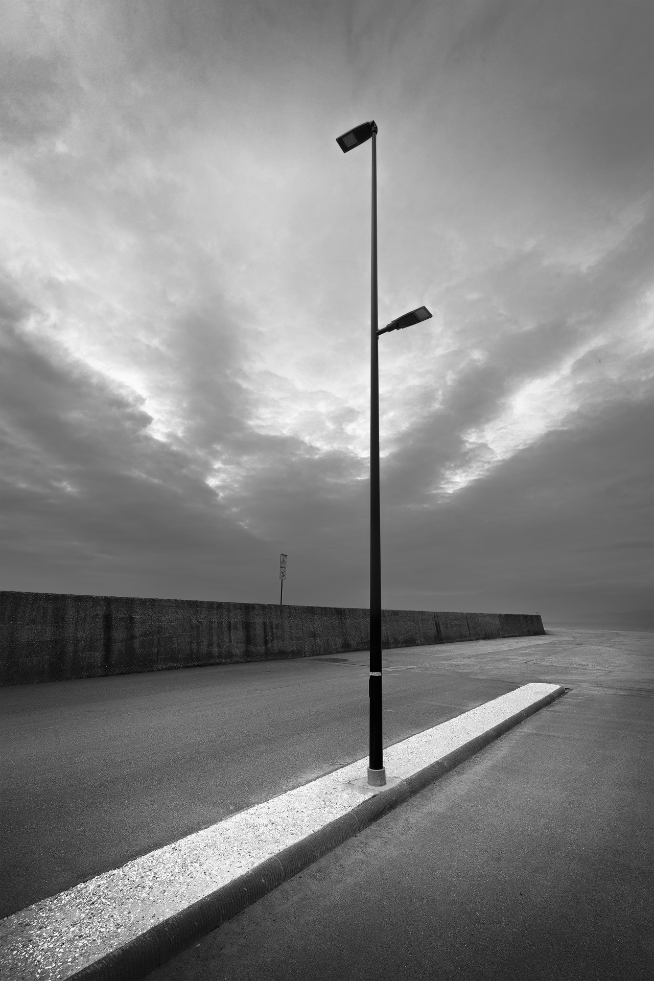 Black and white minimalist photograph of an urban street lamp against a dramatic sky, symbolizing solitude and geometric contrasts.