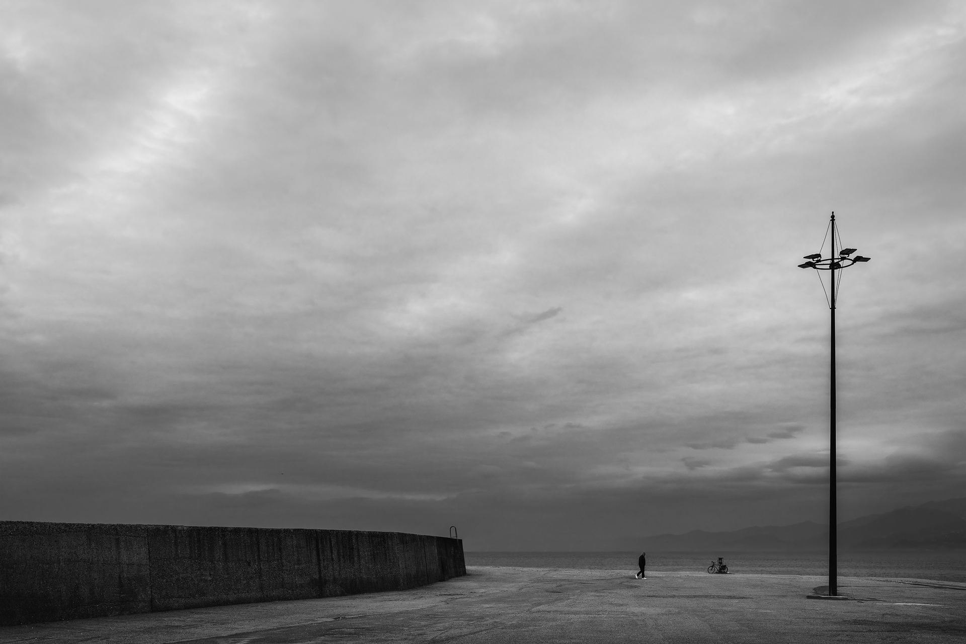 Fotografia minimalista in bianco e nero: un uomo cammina verso l’ignoto in un paesaggio urbano desolato.