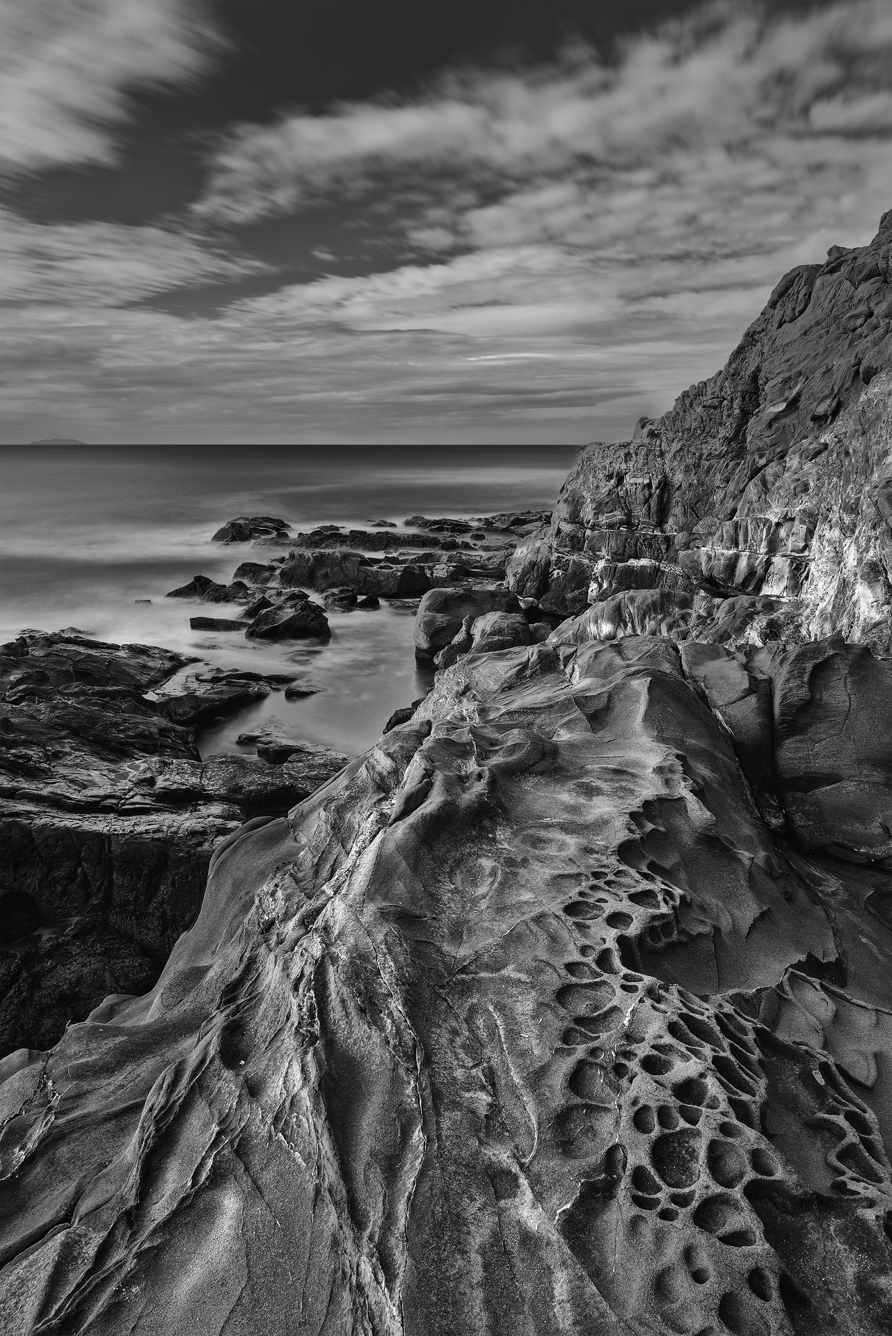 Formazioni rocciose con texture uniche, modellate dal vento e dal mare. Il cielo carico di nubi aggiunge un senso di drammaticità alla scena.