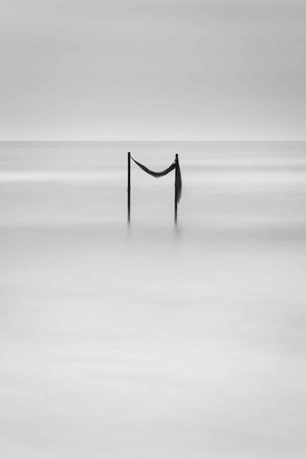 Pali di legno che emergono dall’acqua, avvolti dalla nebbia. Un tessuto consumato dal tempo si agita leggermente, creando un’atmosfera eterea.