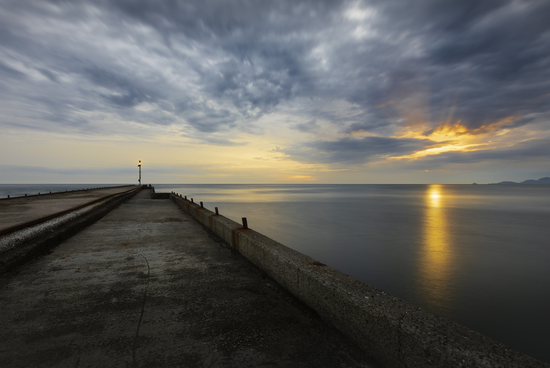 Tramonto sul Mar Ligure al Cinquale con molo in cemento che conduce verso il mare calmo e riflessi dorati tra le nuvole