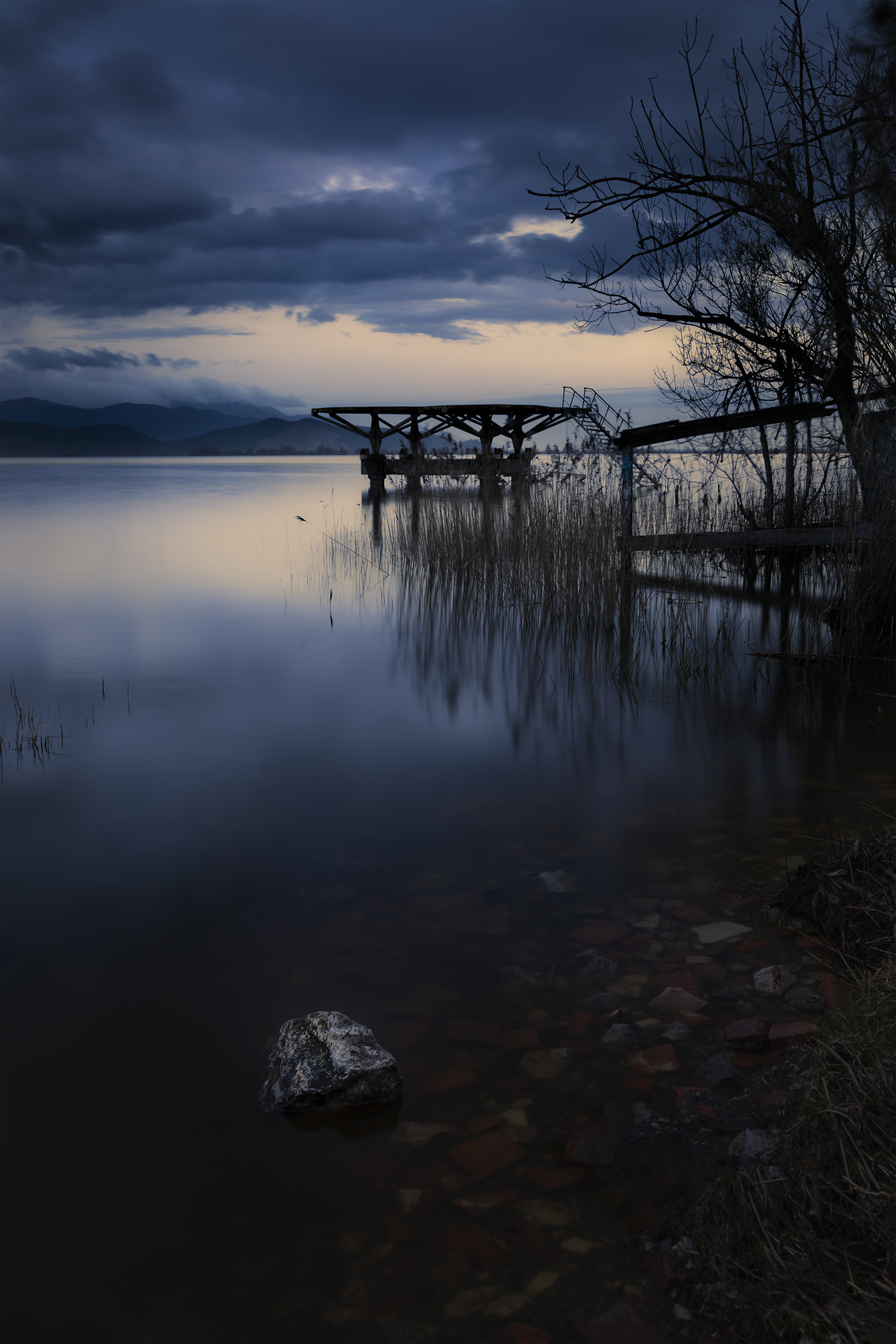Piattaforma abbandonata al tramonto sul lago a Torre del Lago, Lucca, Italia, con cielo nuvoloso e riflessi malinconici sull’acqua