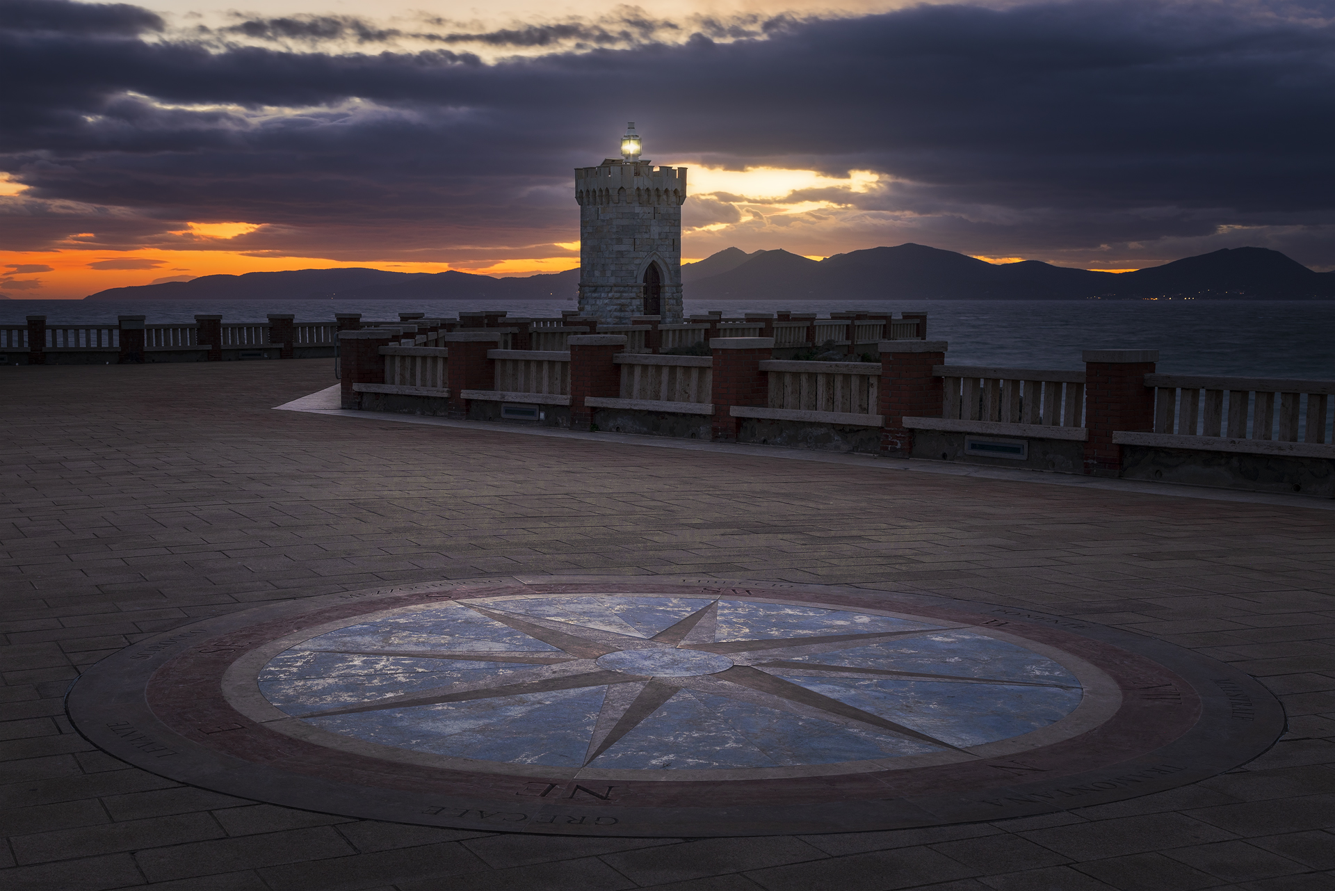 Vecchia torre di avvistamento illuminata dal sole al tramonto. Il pavimento decorato con una rosa dei venti aggiunge profondità alla scena.